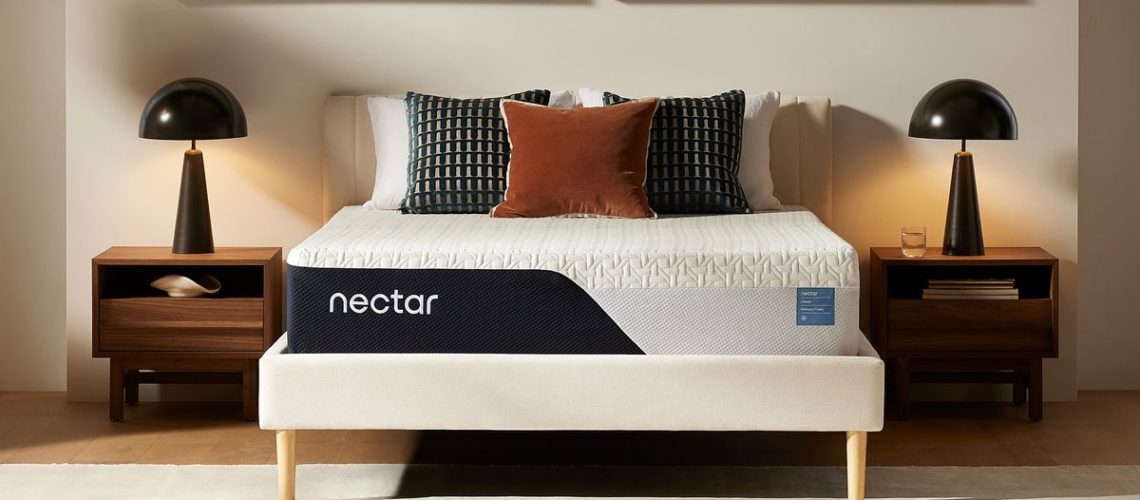 The new Nectar Classic Mattress shown on a white bedframe, dressed with orange, and black and white pillows