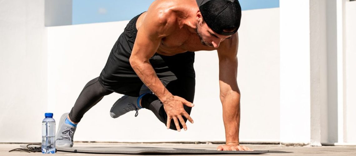 Man in a plank position with right arm and left leg lifted during an outdoor workout