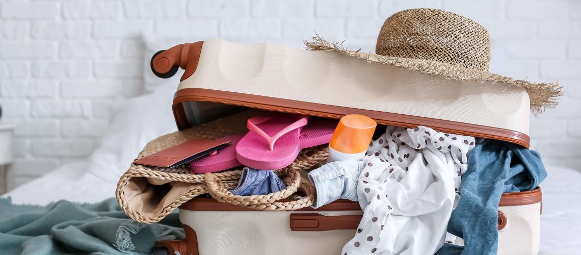 Open suitcase on a bed filled with holiday clothes