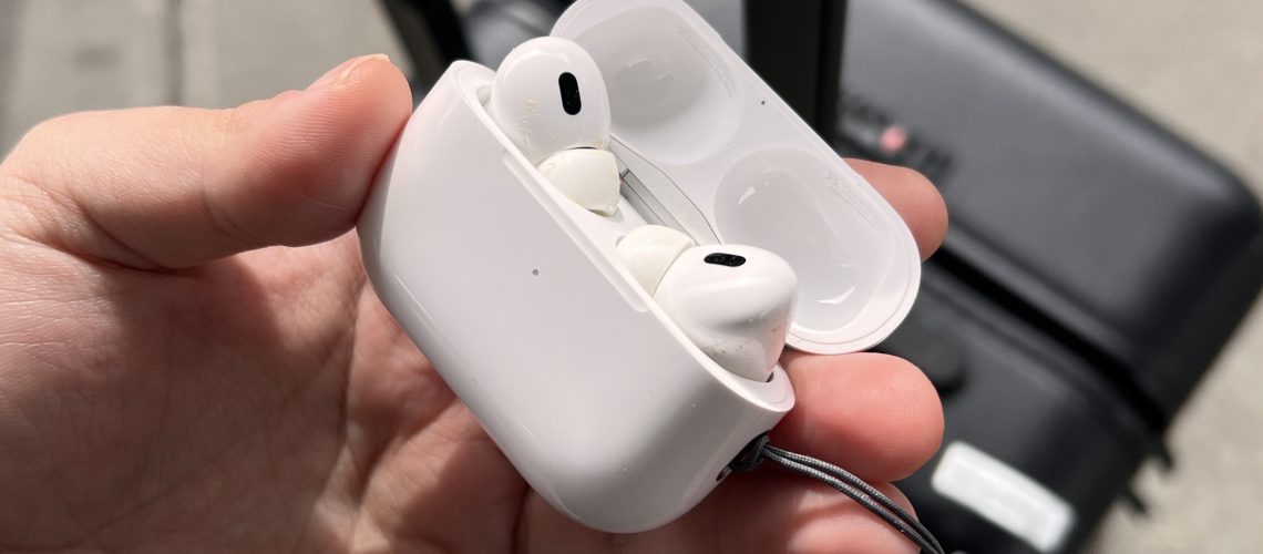 AirPods Pro 2 in a person's hand with the case open in front of luggage