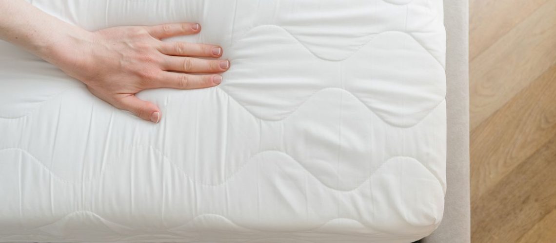 A person places their hand on one side of their white mattress to check for signs of dipping and sagging