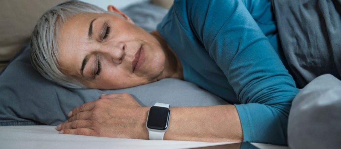 Woman sleeping on her side with a smart watch on her wrist and her phone on the bedside table