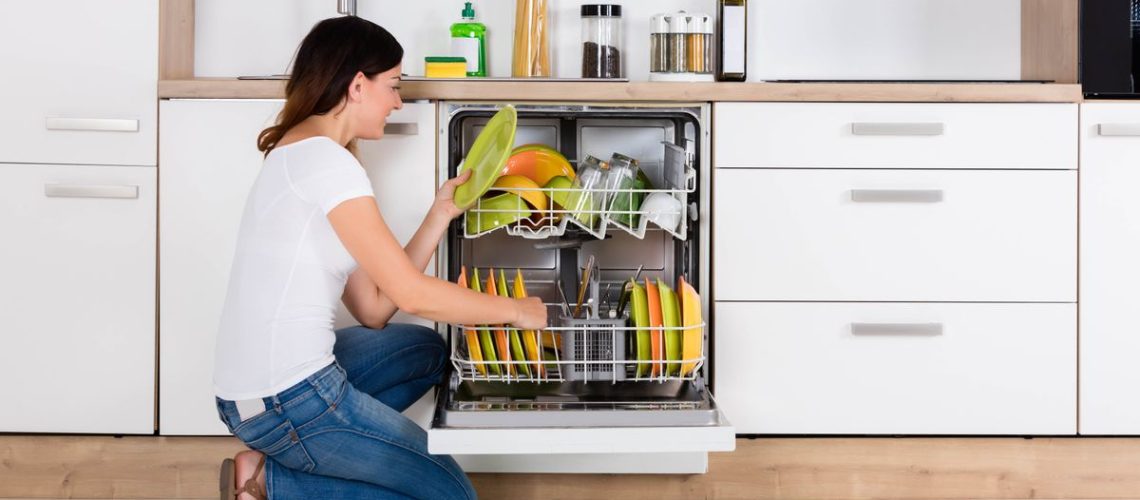 A woman emptying a dishwasher filled with colorful plates