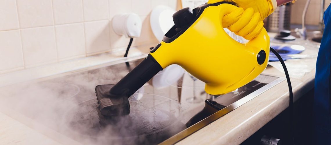 A yellow steam cleaner being used on an electric cooktop