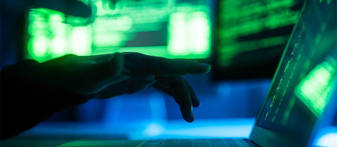 Hacker typing on laptop in darkened room