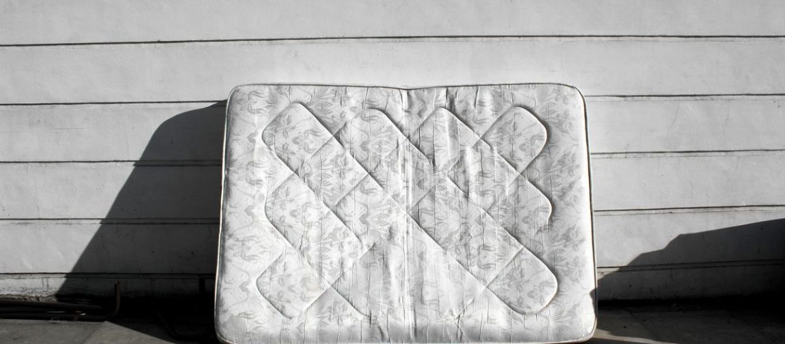 An old mattress leans against the side of a building