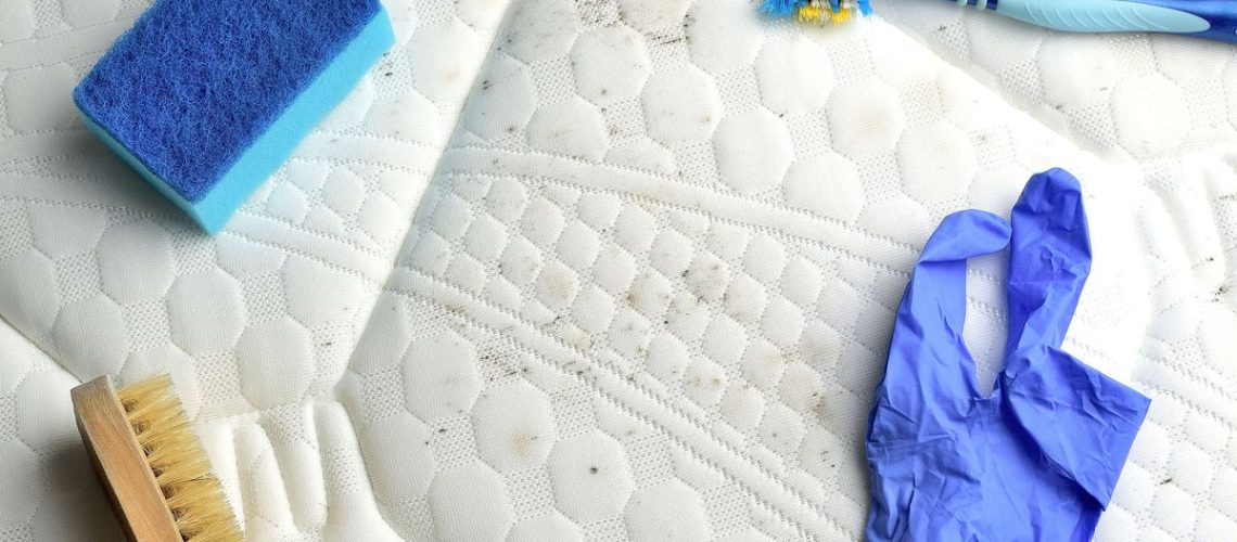 Image shows black mold on a white mattress being cleaned with alcohol, brushes and sponges