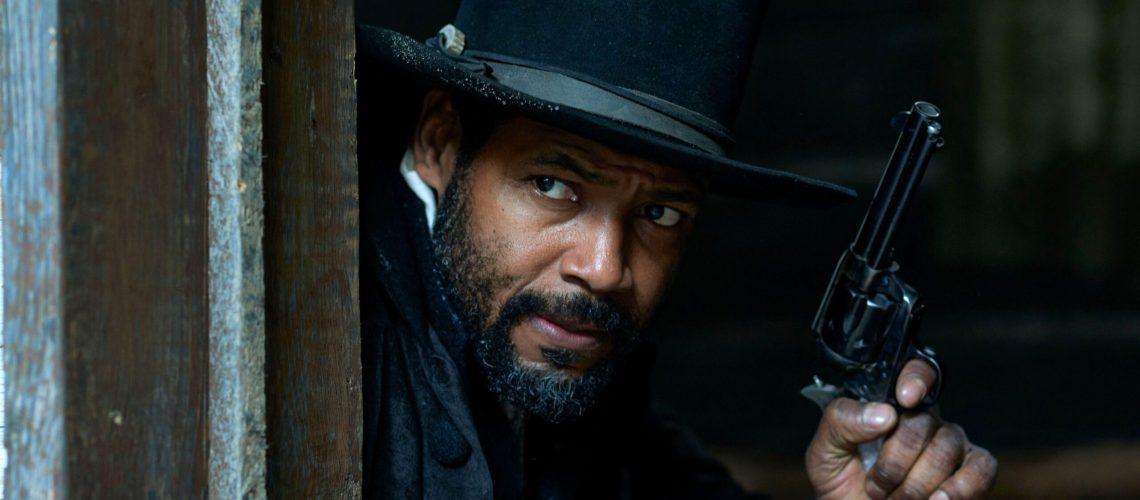 Cicero (Isaiah Mustafa) peers round a door frame, gun readied, in a scene from "Murder at Yellowstone City"