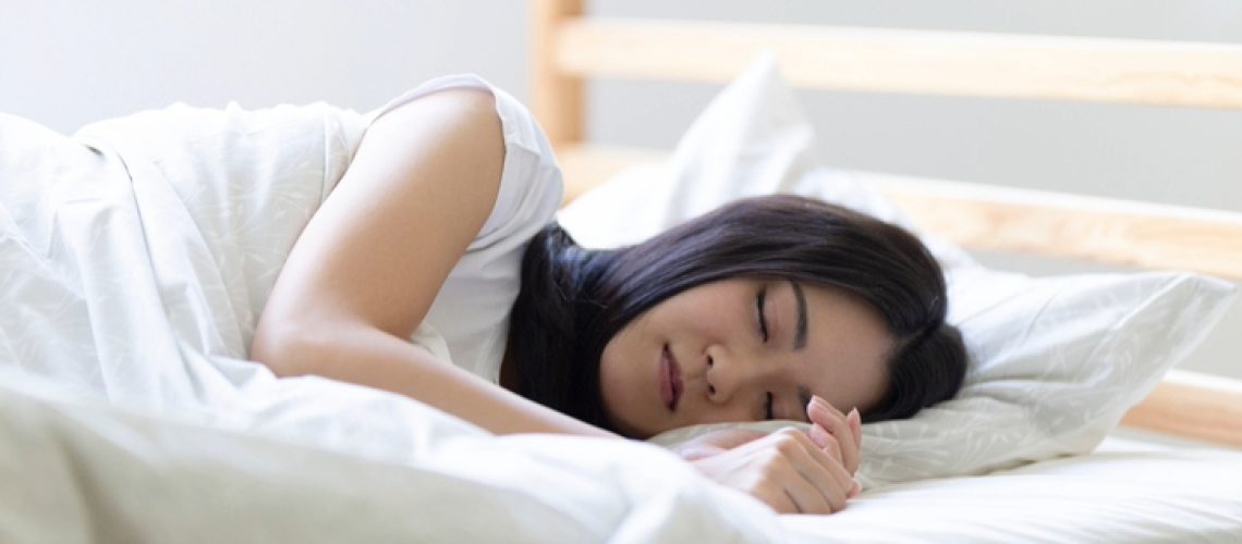 A woman with dark hair sleeping on her side in bed with white bedding