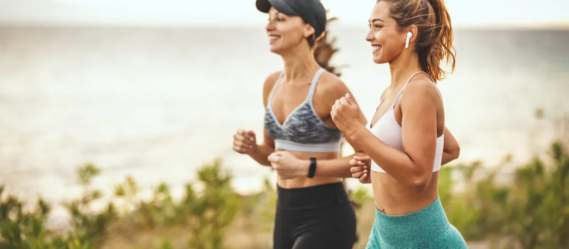 Two women power walking outdoors by the ocean smiling