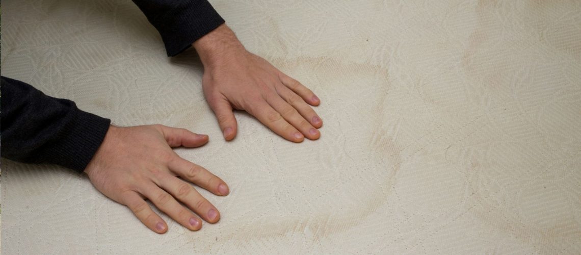 The image shows a person placing their hands on a sweat stained mattress