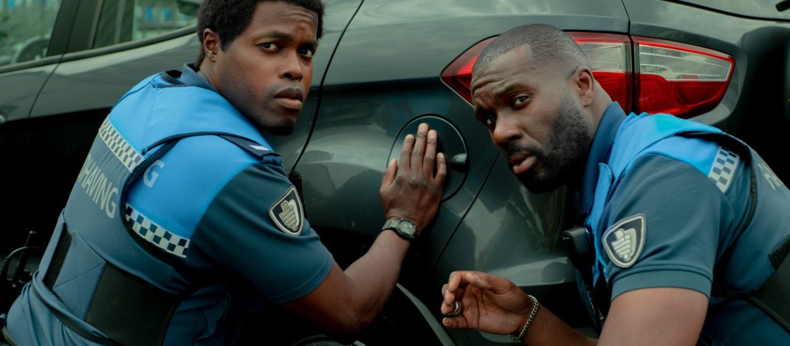 L-R: Ramon and Jack crouch beside a car in a scene from Netflix's "Almost Cops"