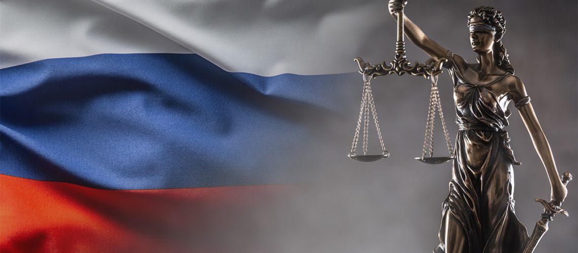 Bronze legal stature holding scales, with Russian flag behind it