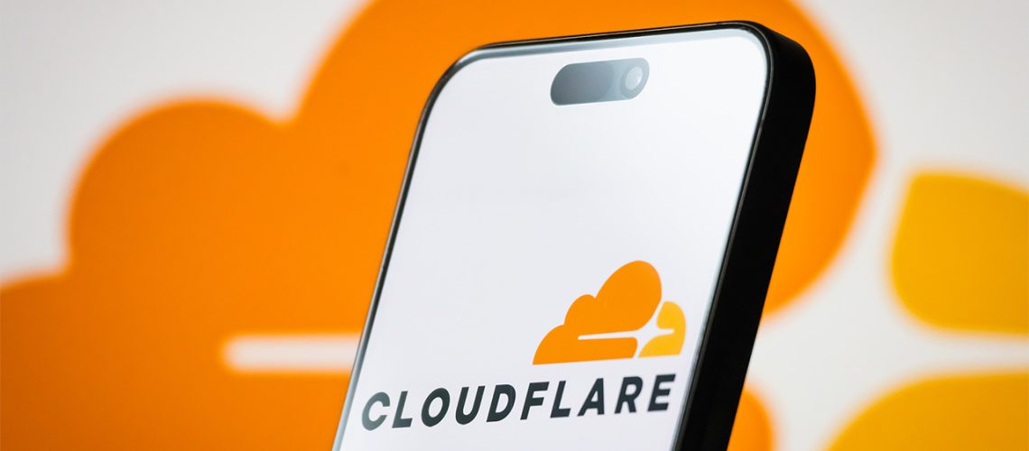 Orange Cloudflare logo displayed on smartphone. There is an orange cloud with black text and a larger orange cloud in the background