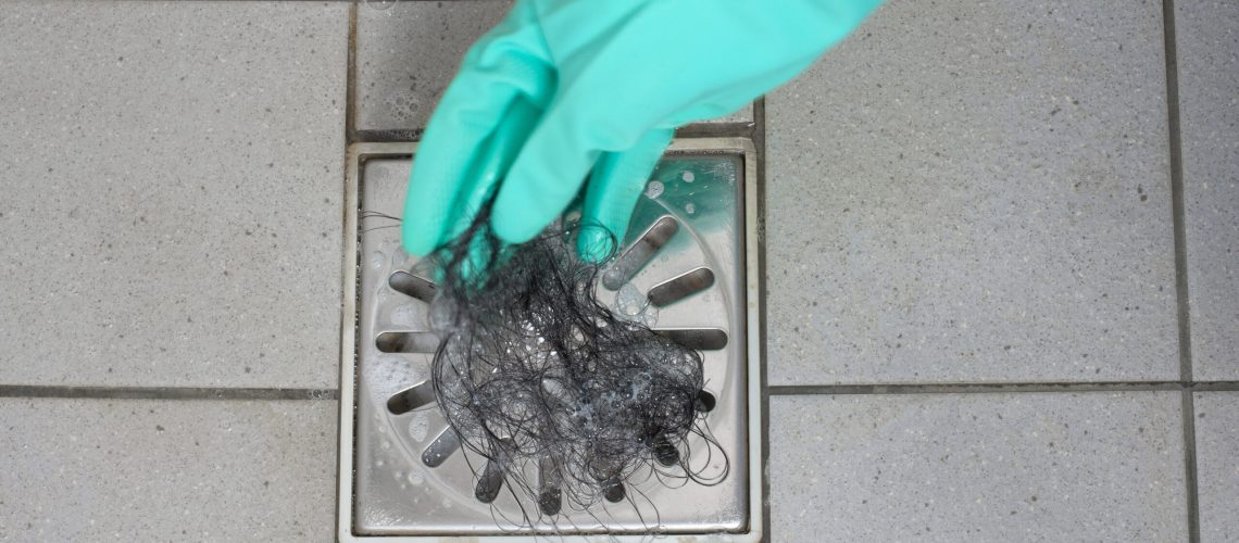 A gloved hand removing hair from a shower drain