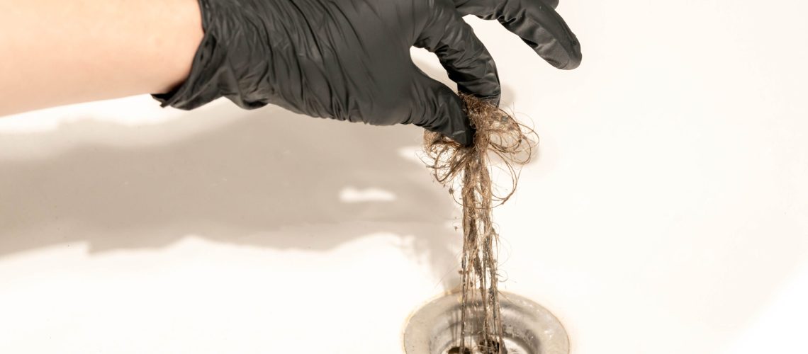 Shower drain being unclogged with a gloved hand