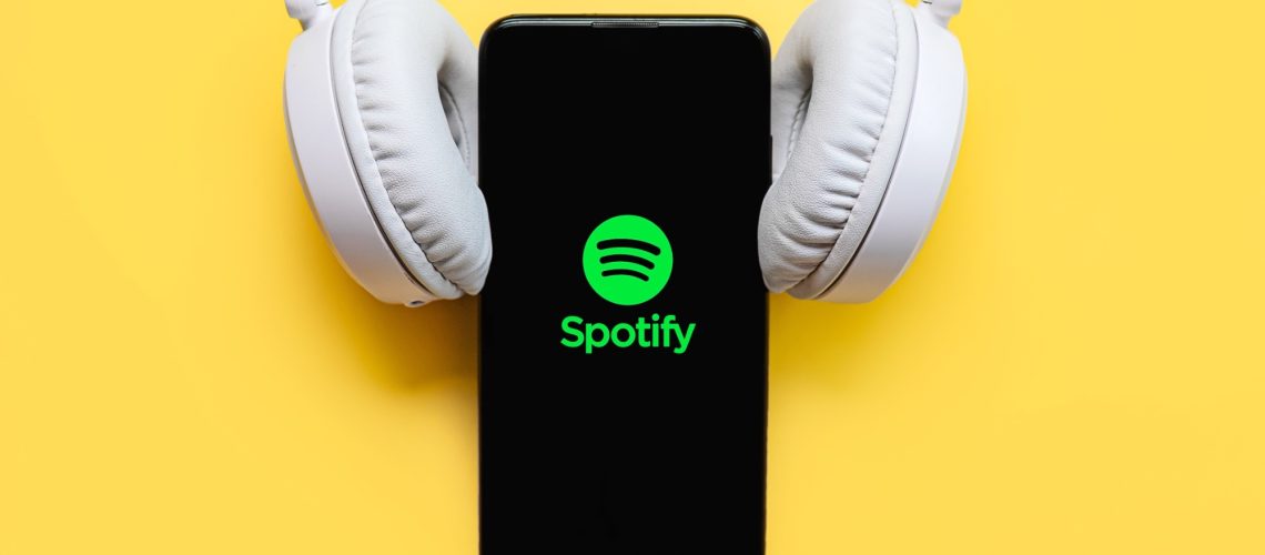 Spotify logo on a phone with white headphones resting on the phone