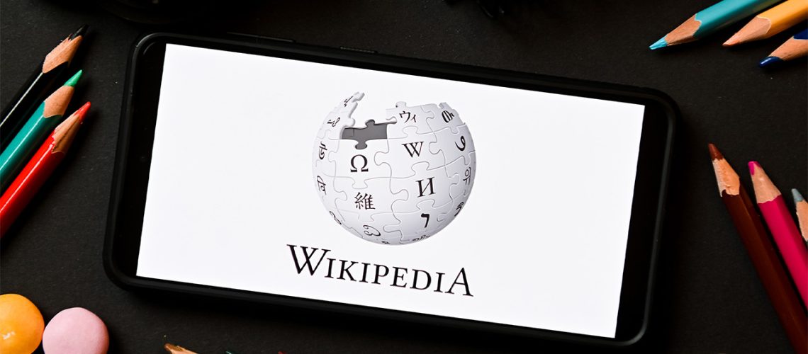 Wikipedia logo on smartphone with coloured pencils surrounding it