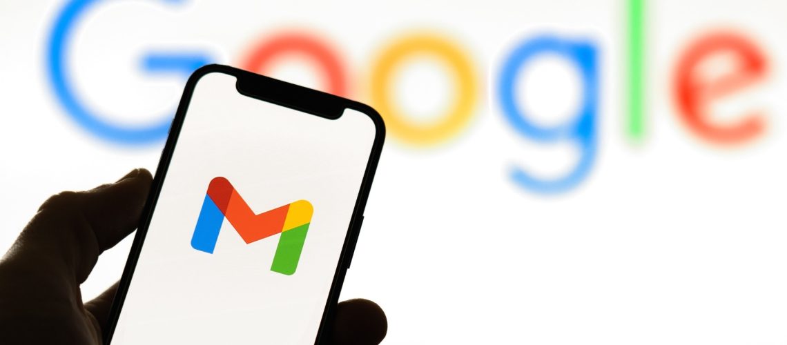 A smartphone with the Gmail logo on it, being held by a hand, in front of a Google background
