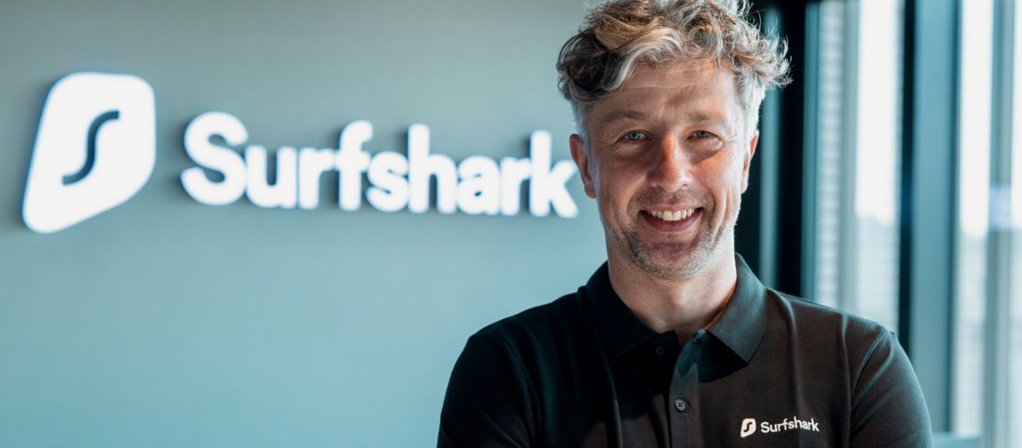 Headshot of Vytautas Kaziukonis, Surfshark CEO, with a neon Surfshark logo in the background.