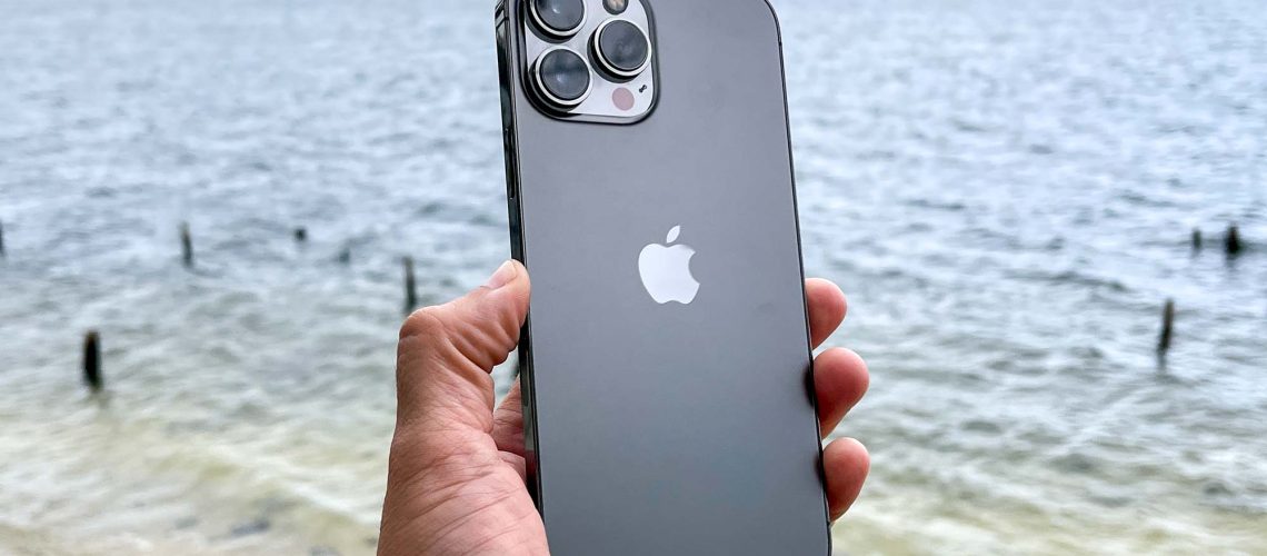 iPhone 13 Pro Max in grey, held in front of water