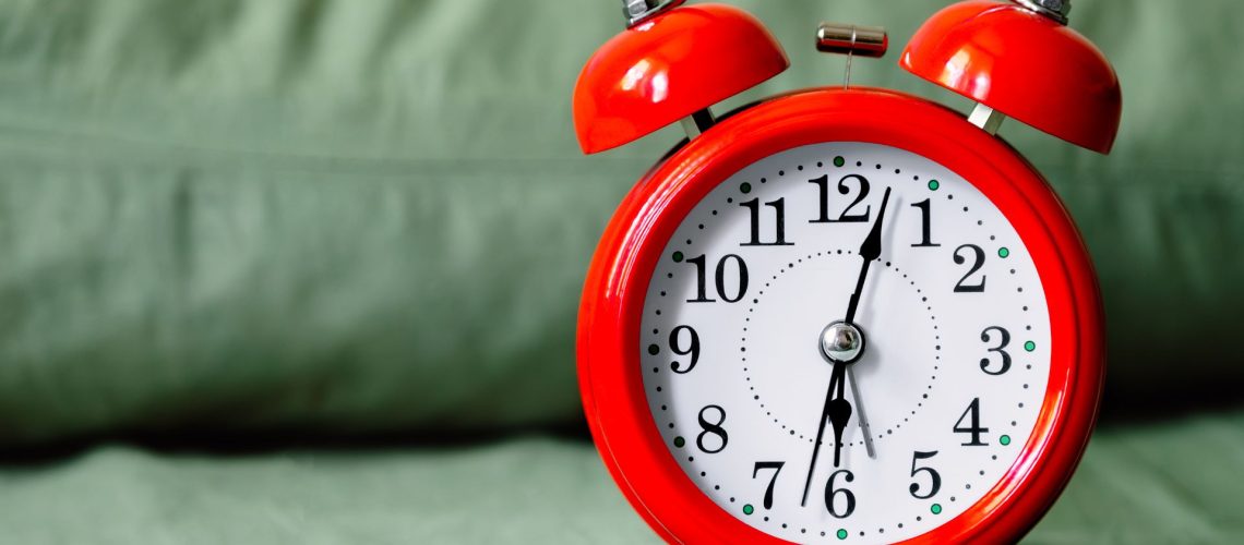 A red alarm clock placed on a light gray/green bed.