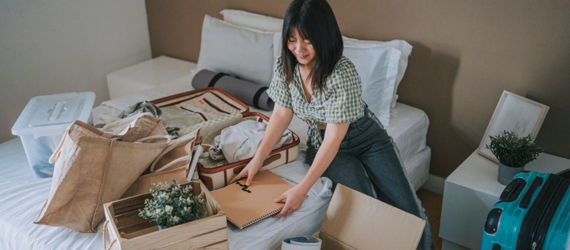A woman sat on her bed decluttering her bedroom, tidying away boxes and items as well as suitcases
