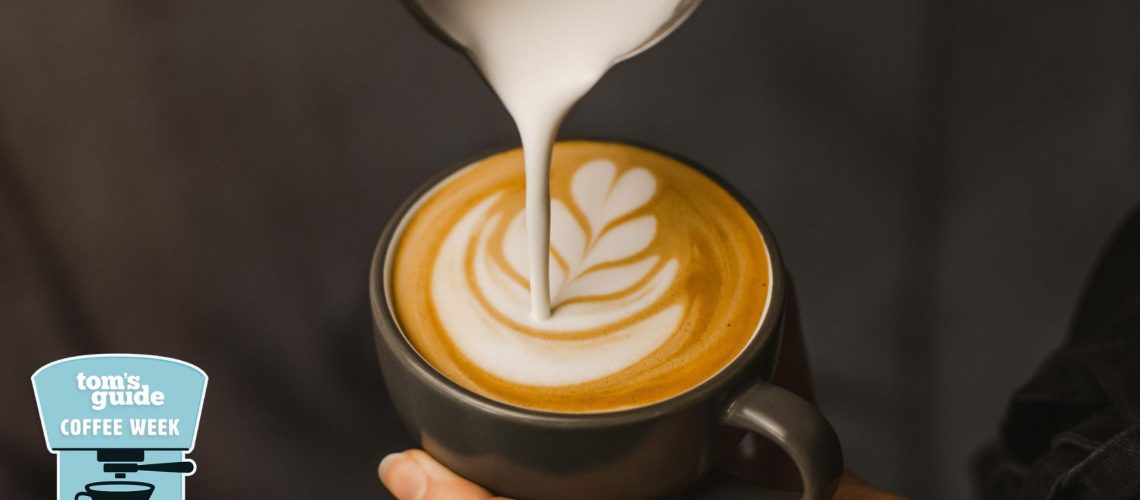 A person doing latte art in a black coffee mug