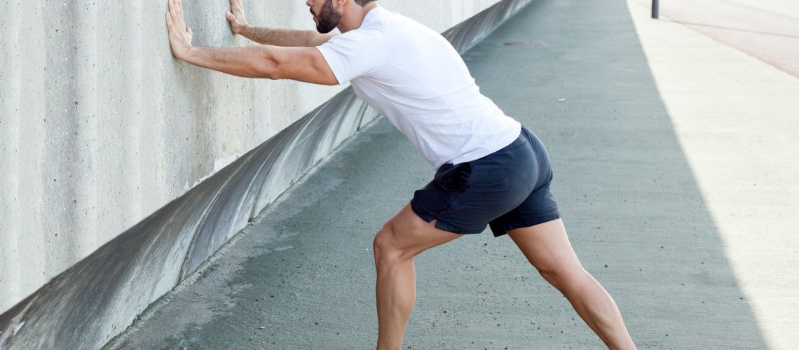 Man with arms pressed on a wall left leg forward and right leg back in a high lunge