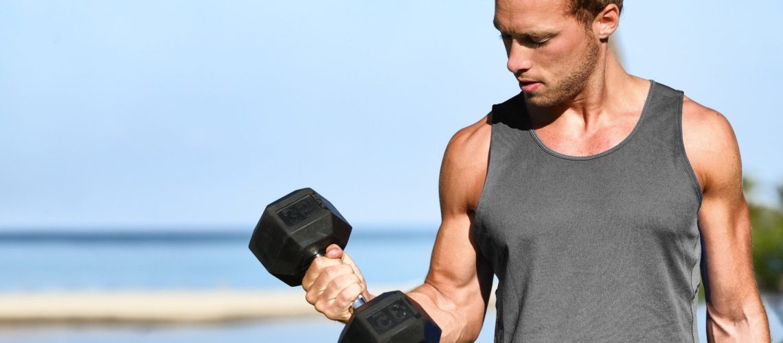 Man holding a dumbbell in right hand with elbow flexed during arm workout outdoors