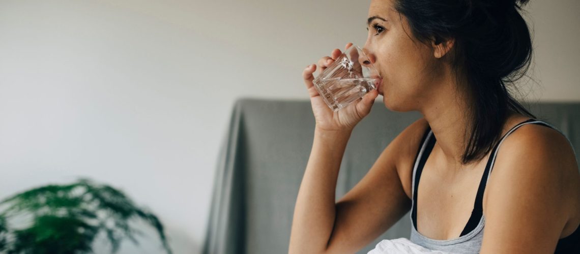 A woman sits in bed drinking a glass of water.