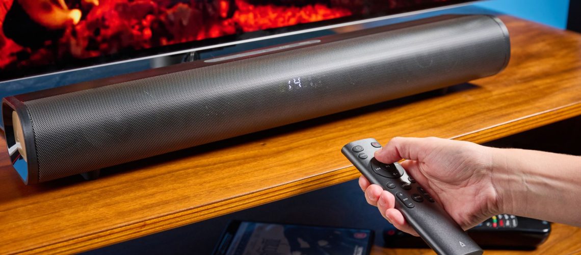 the creative stage pro soundbar and subwoofer, a super-budget home cinema system with 2.1 channels and a remote control photographed on a wooden tv stand with a TV behind