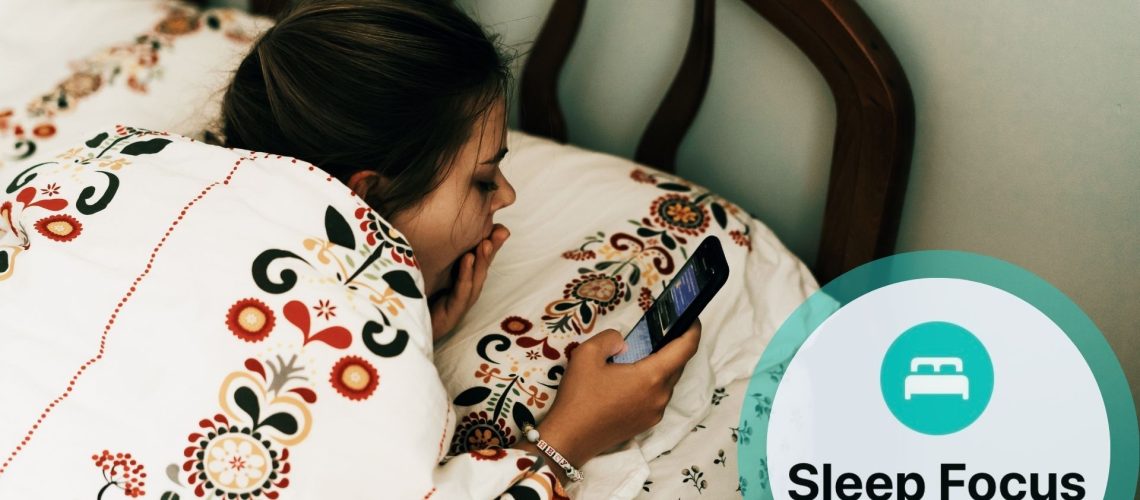 A young girl in bed with tapestry pattern sheets, laying on her front using a mobile phone as she yawns. With inset of Apple Sleep Focus logo