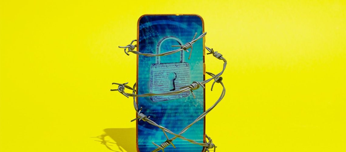 Image of smartphone wrapped in barbed wire. The screen displays a padlock and the phone is in front of a yellow background