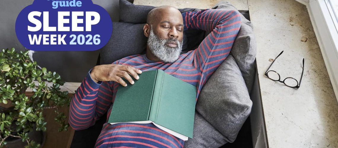 A man in his late 60s, dressed in a striped red and blue sweatshirt, takes a nap on the couch after reading a book. He has no idea that his long daytime naps as the reason why he keeps waking up at 3 a.m. A blue Tom's Guide sleep week logo sits in the top left hand corner.