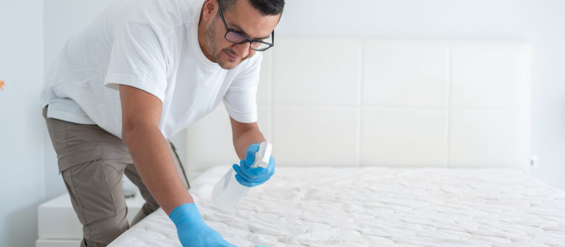 A man cleaning a mattress with a spray bottle and cloth.