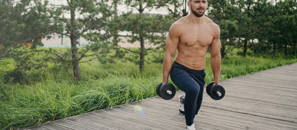 Man outdoors performing lunge with set of dumbbells on a walkway in nature
