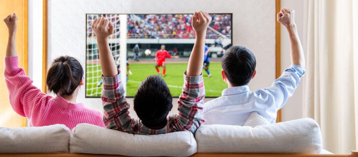 Family watching television and cheering soccer game on TV together in their living room.