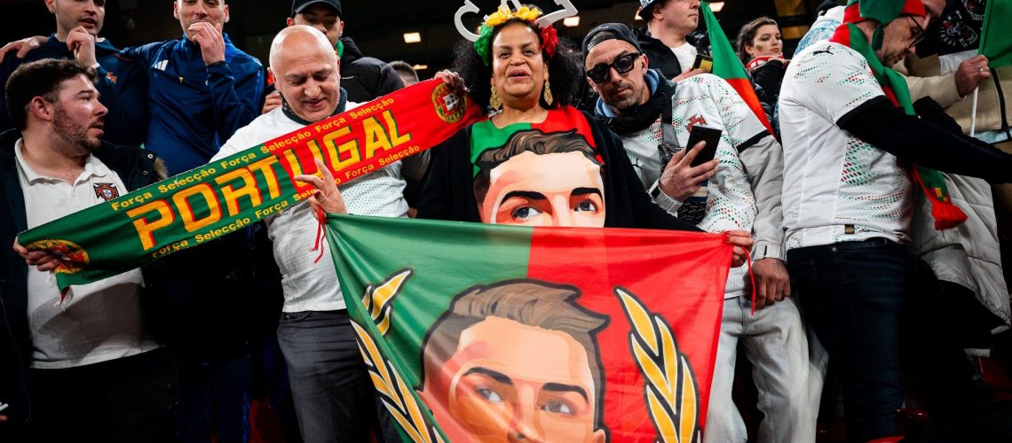 Woman seen wearing a CR7 - Cristiano Ronaldo shirt and holds flag with his portrait while surrounded by other soccer fans during a Portugal match.