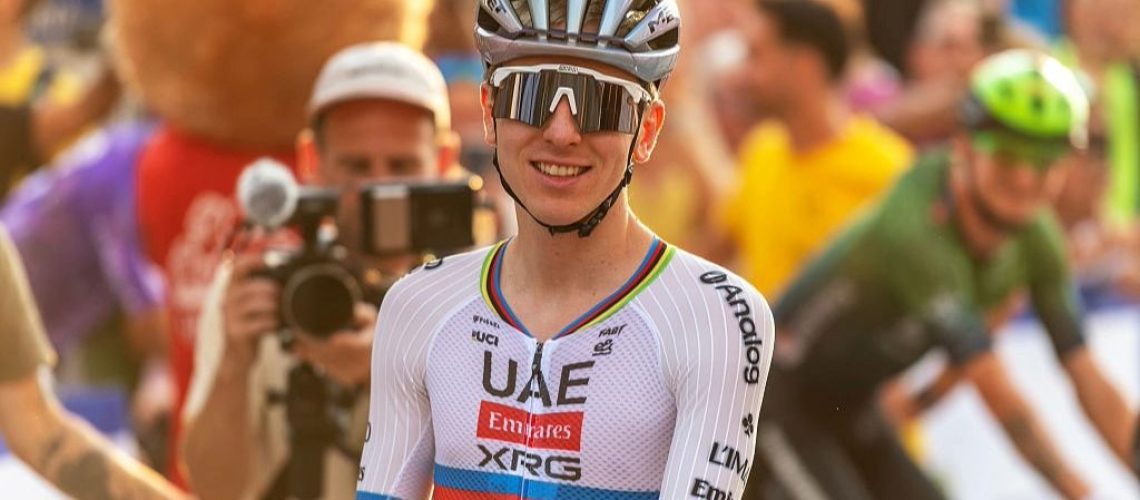 Tadej Pogacar, wearing a cycling helmet and rainbow colors of the world champion, smiles at the end of a cycling race.
