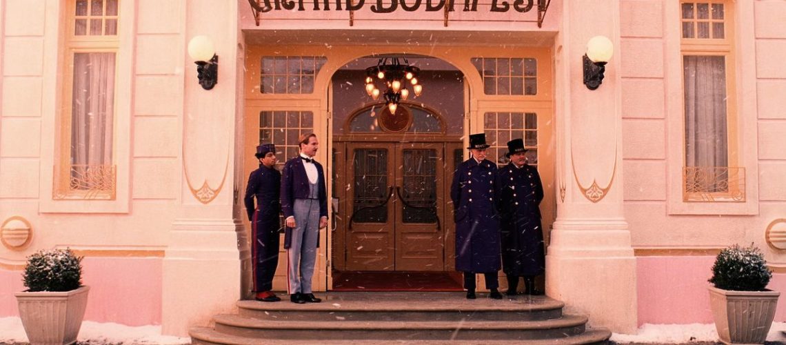 Zero (Tony Revolori) and M. Gustave (Ralph Fiennes) stand on either side of the doors to The Grand Budapest Hotel