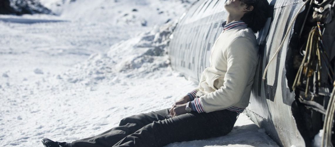 Enzo Vogrincic Roldán as a despondent Numa Turcatti sitting on a snowy mountaintop against the crashed remains of a commercial airplane in Society of the Snow