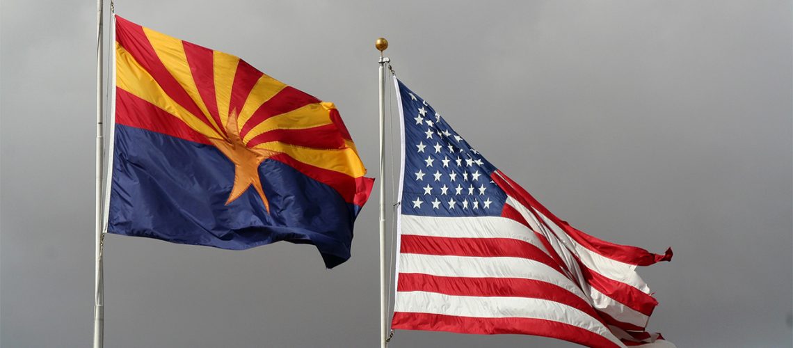 Flags of Arizona and US flying in front of grey storm clouds