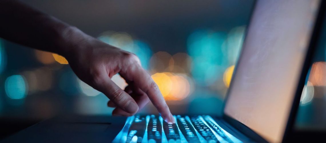 A person typing on a computer, lit up by the screen