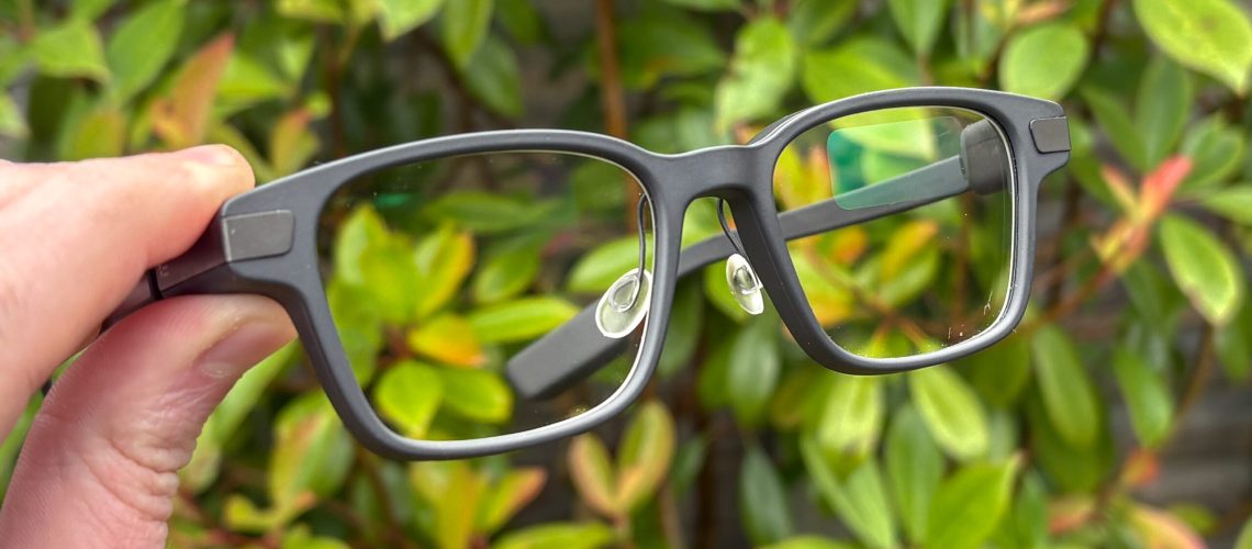 Even Realities G1 Smart Glasses held by fingers with green bush in background