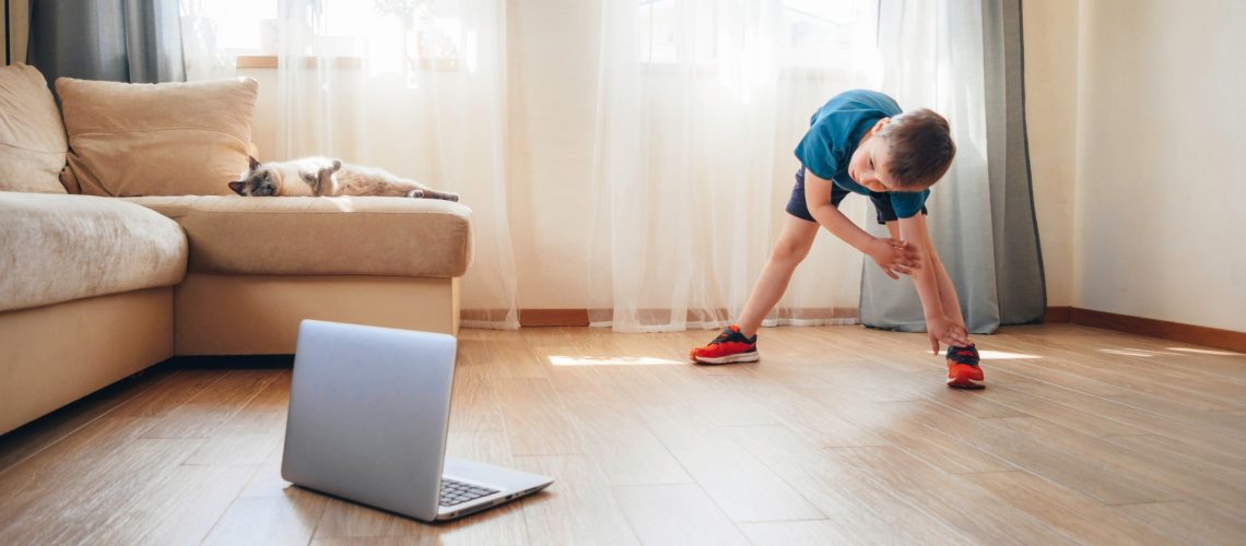 The boy doing physical exercises, watching video lesson online in front of open laptop computer