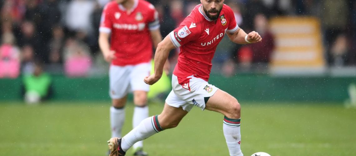 Elliott Lee on the ball for Wrexham in the red shirt and white shorts home strip.