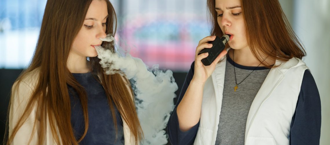 Two young girls smoke electronic cigarettes