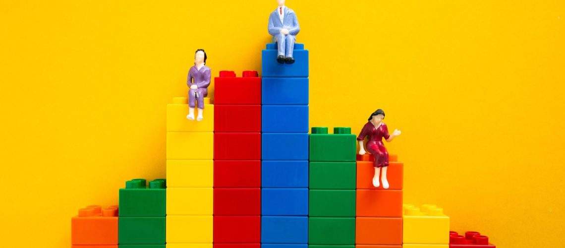 Concept of inequality: plastic figures sat on Lego blocks of different heights
