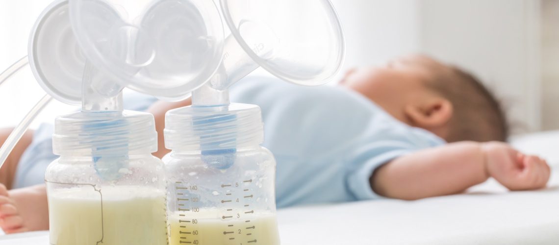 Breast milk pump and baby lying on the white bed